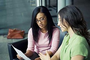 Zwei junge Frauen blicken auf ein Blatt Papier und diskutieren darüber